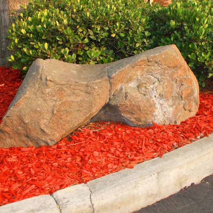 Red mulch under a large rock by curb