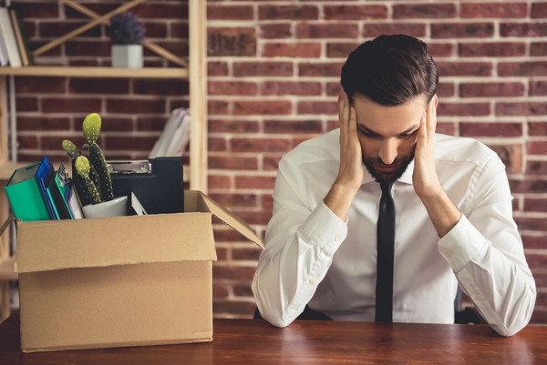  A businessman is upset and packing his things into a box at his desk.