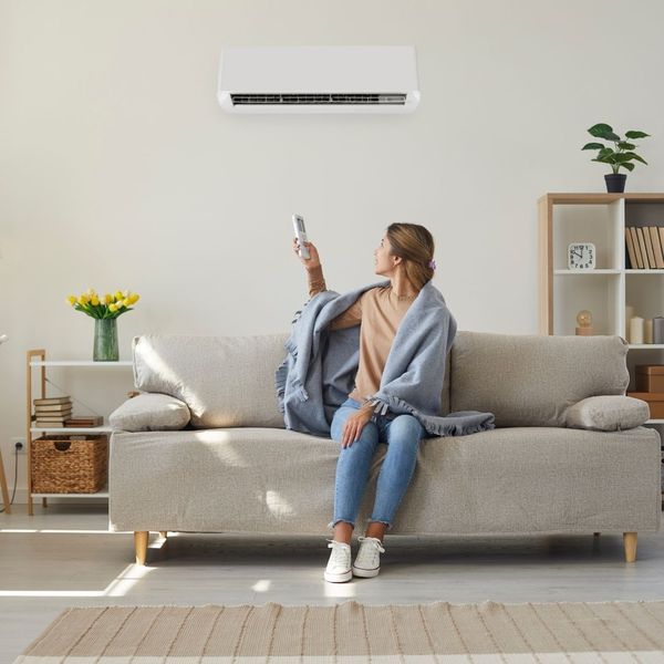 a woman sitting on her couch adjusting the thermostat with a remote