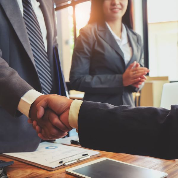 People in suits shaking hands with woman in background