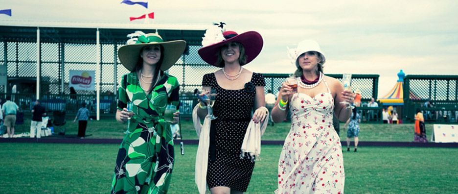 Three women in dresses and hats holding drinks
