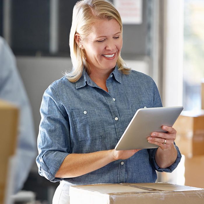 smiling warehouse manager next to boxes using a tablet