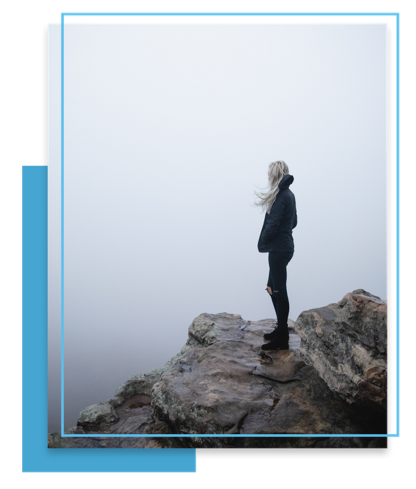woman standing on mountain looking out at fog