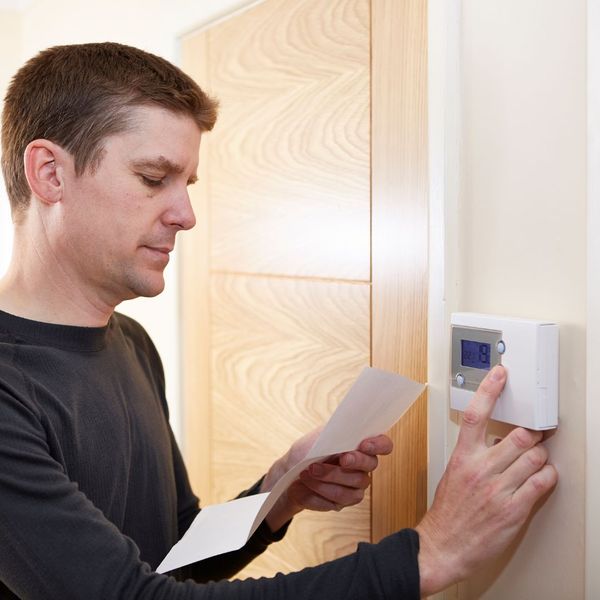 man looking at energy bill and lowering thermostat
