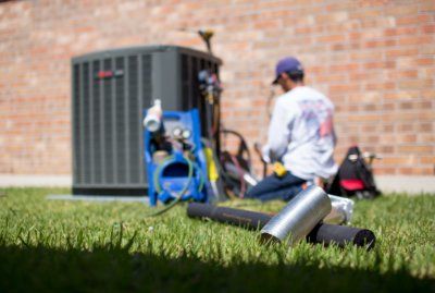 HVAC technician working on air conditioning unit next to red brick building home.jpg