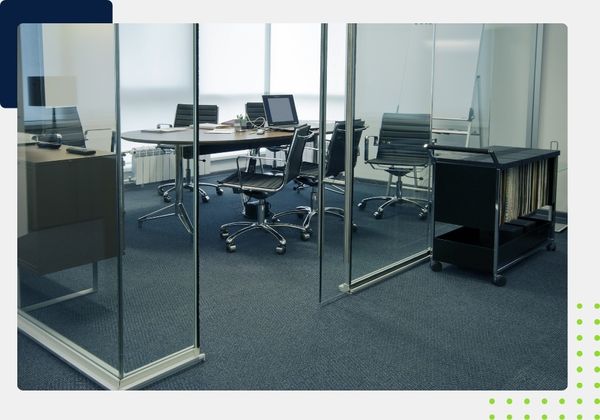 A clean, modern conference room with a large oval table, office chairs, and glass walls. The carpet is a dark, patterned blue.