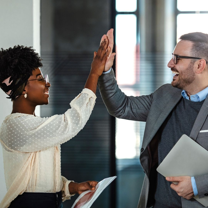 A man and a woman in business attire high five while holding printed documents