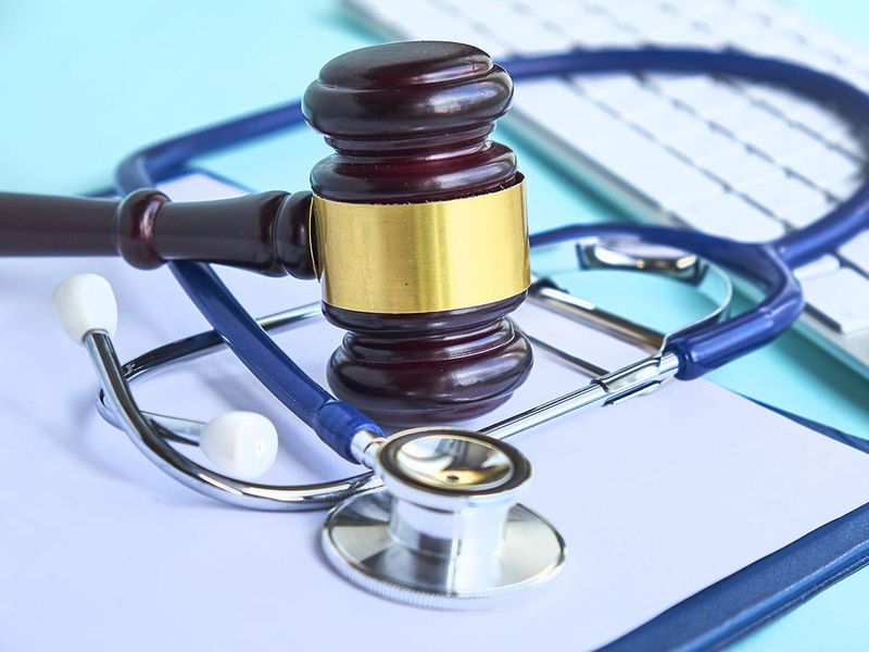Gavel on top of a stethoscope on top of a blue clipboard next to a keyboard