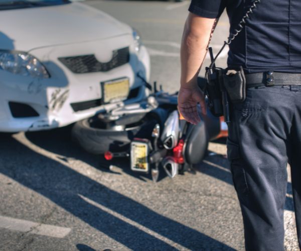 a police officer standing in front of a wrecked motorcycle and car 