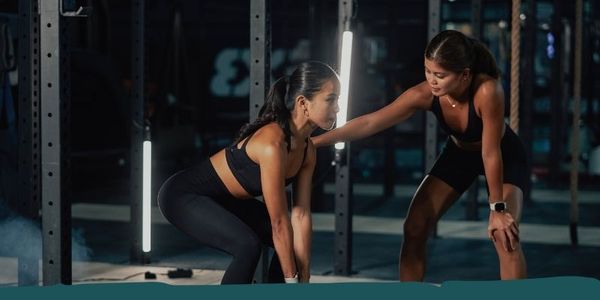 Personal trainer correcting a female client's squat form in a gym.