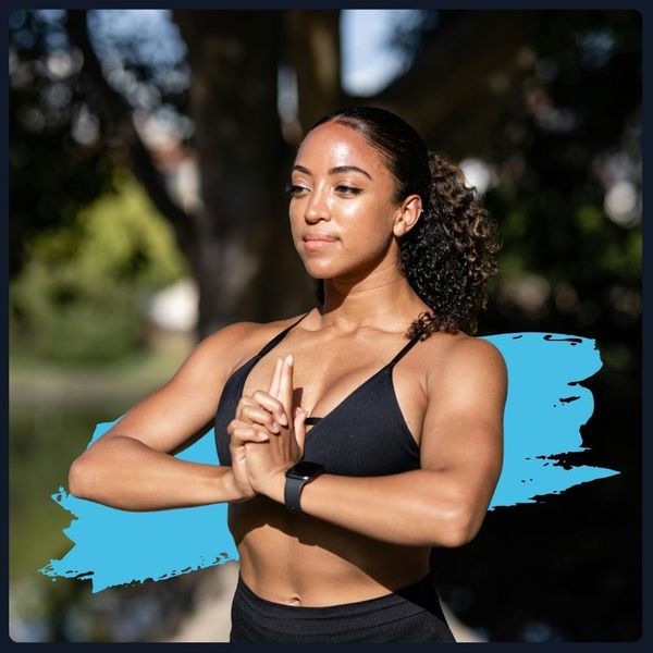 Fit woman in a black sports bra, meditating or posing outdoors.