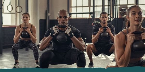 Group of people doing a kettlebell squat exercise in a gym.