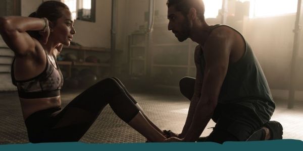 Man assisting a woman with a sit-up exercise, one-on-one training.