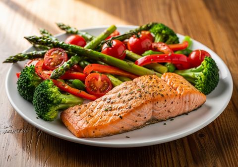 A nutritious meal featuring grilled salmon and fresh greens sits on a sunlit wooden dining table.