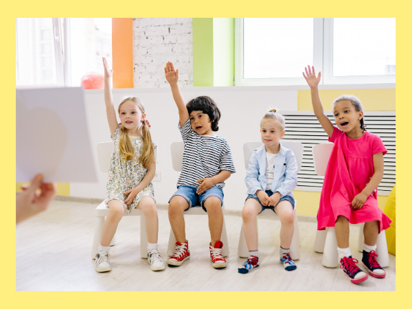 children sitting down raising their hands. 