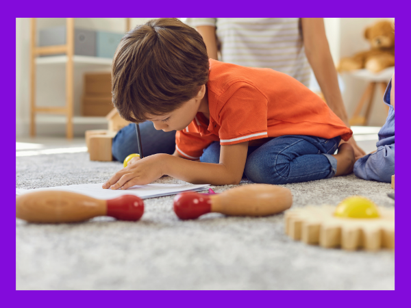 child surrounded by toys writing something on a piece of paper. 