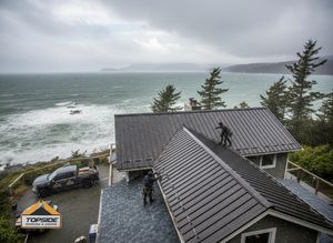 Roofers installing metal roofing on a coastal house during a storm