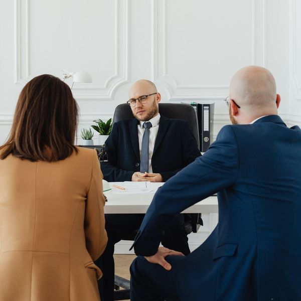 A lawyer sits at a desk with two clients, a man and a woman, facing him, engaged in a serious discussion during a legal consultation.