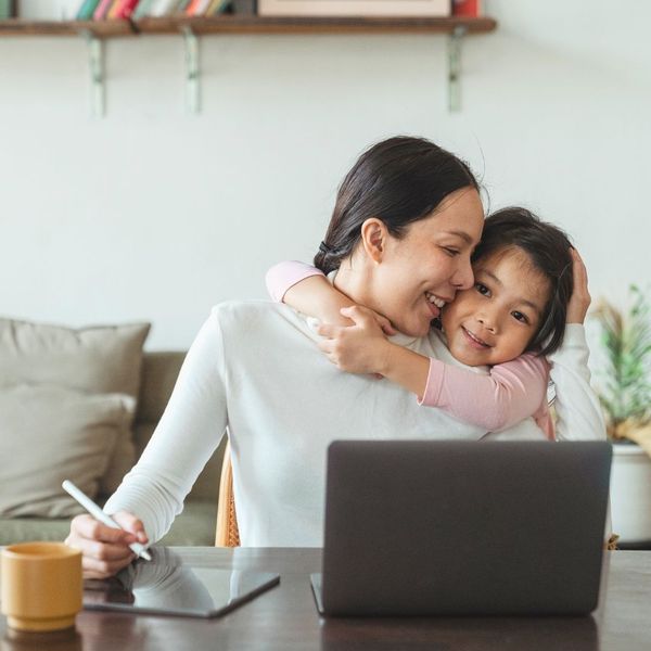 daughter hugging mother from home while she works on a computer and tablet