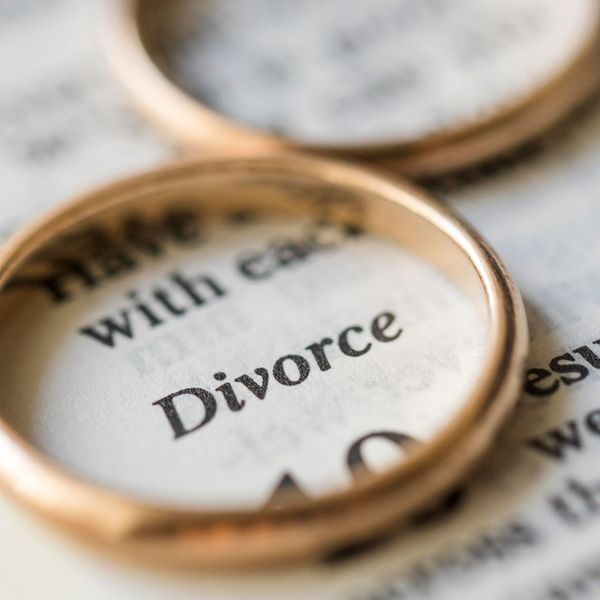 A close-up of two wedding rings resting on an open dictionary page, with the word "Divorce" clearly visible.