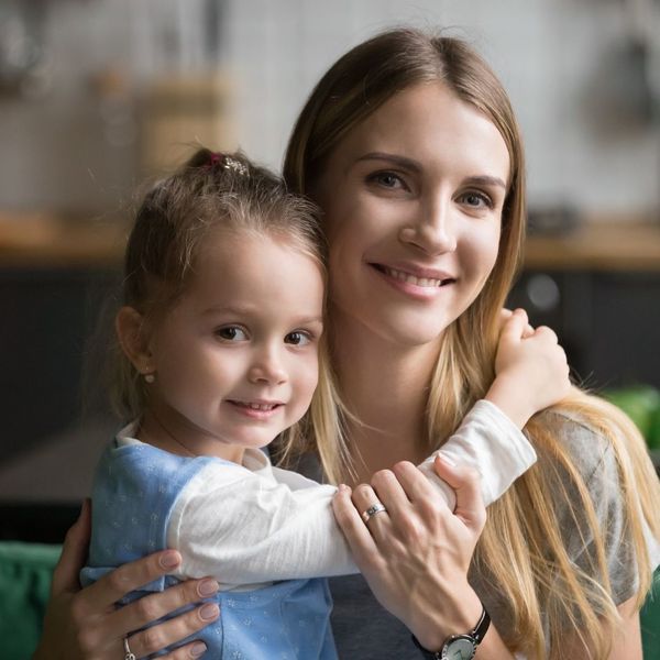 A smiling mother embracing her young daughter, both looking happily at the camera.