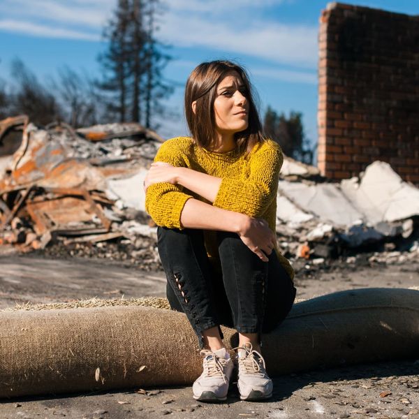 woman sitting outside of burnt down house