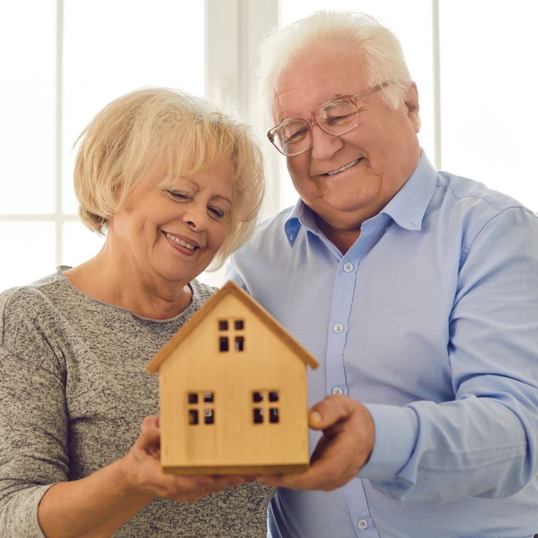 happy elderly couple holding wooden model house