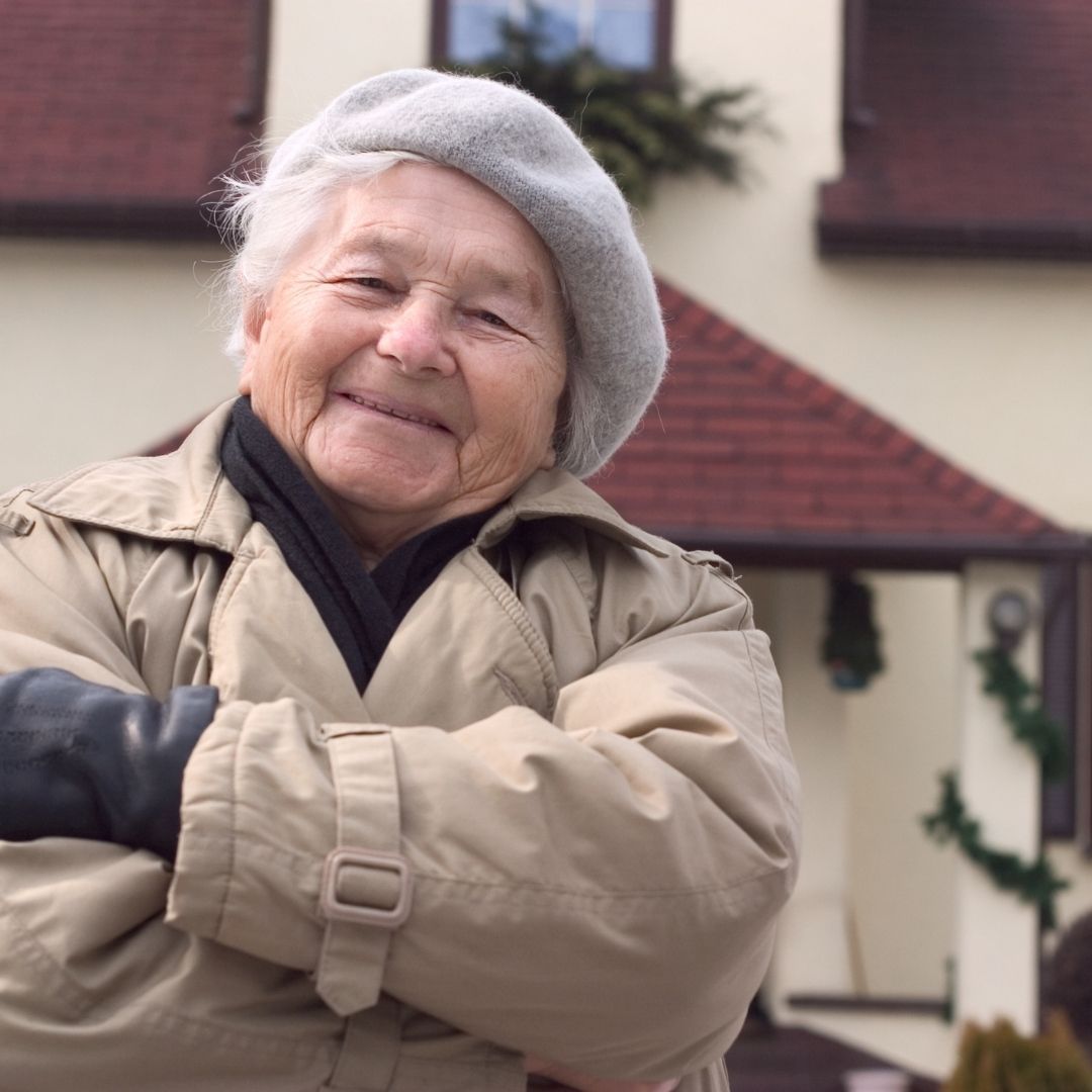 happy woman in coat, arms crossed, in front of house