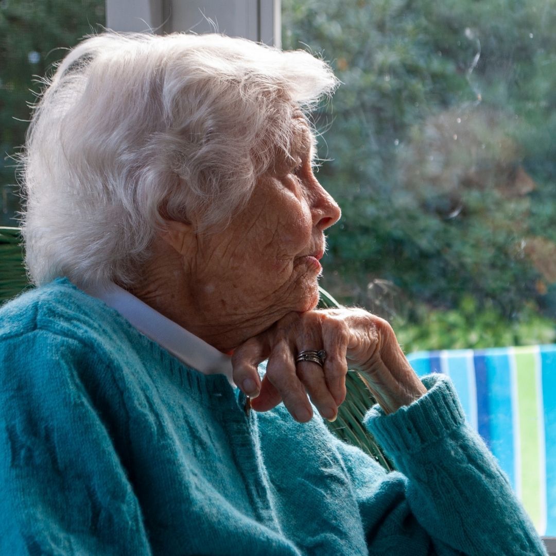 older woman in sunroom, looking wistfully through windows