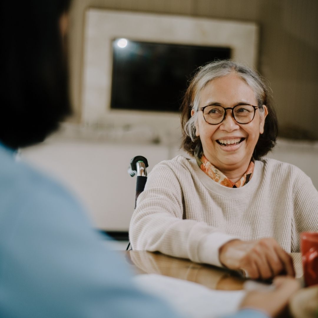 happy older woman talking to person blurred in foreground