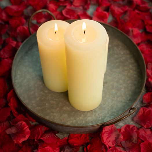 Two candles on a metal plate surrounded by red flower petals