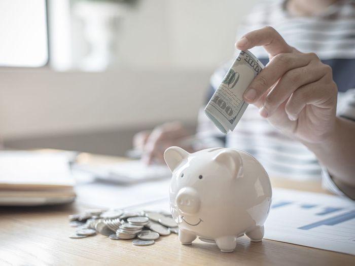 person putting a hundred dollar bill in a piggy bank