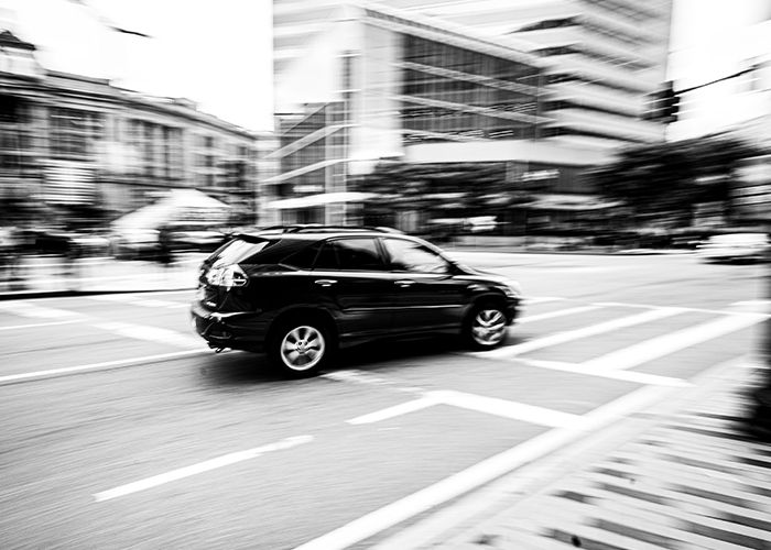 black adn white image of vehicle driving through city streets with blurry background. 