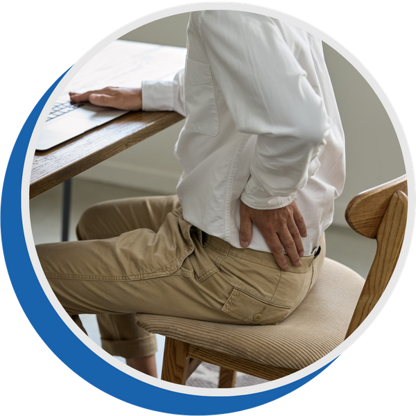 man sits in chair in front of laptop holding back 