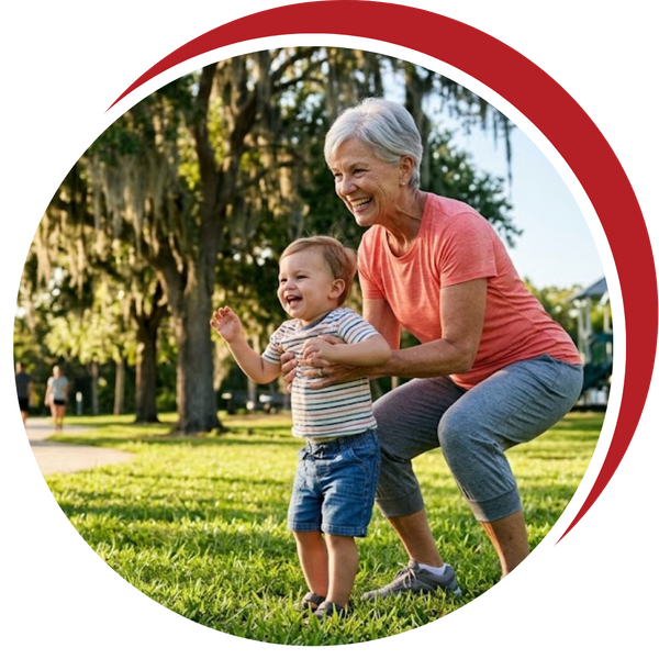 An older woman smiling and playing with a toddler on the grass in a sunny park