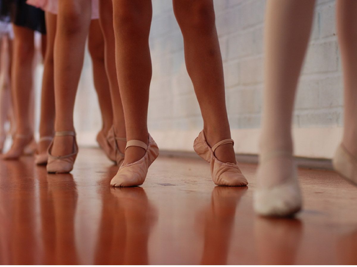 Girls in tights and ballet shoes in first position up on releve.