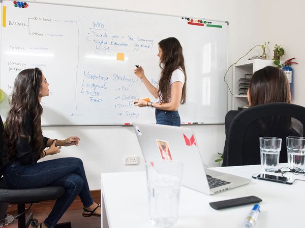 Three women brainstorming in front of a whiteboard. 