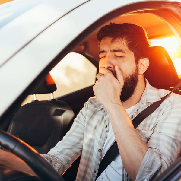 man sitting in drivers seat of car while yawning