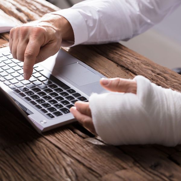 image of man with injured hand  typing on laptop with one finger