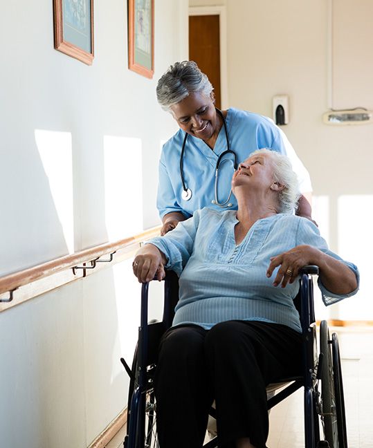A woman in a wheelchair being pushed by a nurse