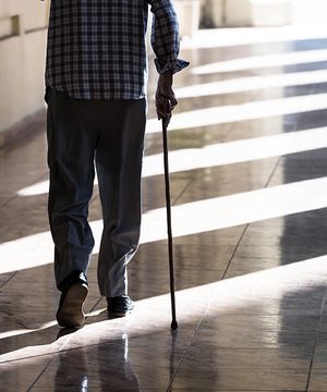 An elderly man with a cane walking down a hallway 