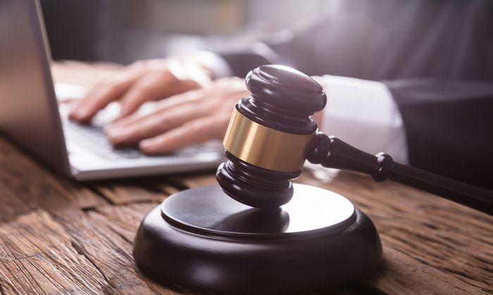 a person typing on a laptop behind a gavel