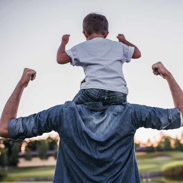 dad flexing his muscles with his son on his shoulders