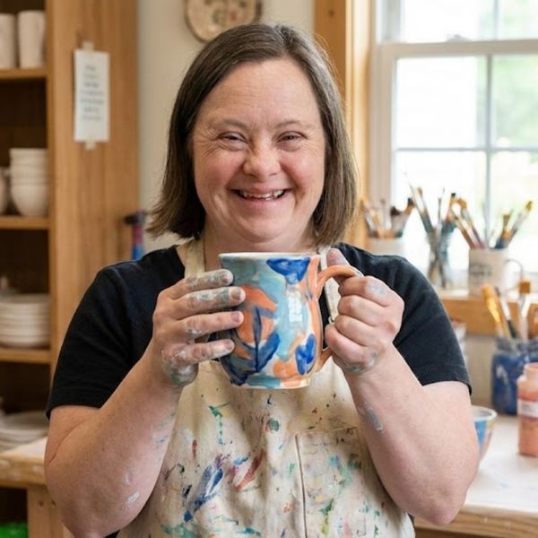 an adult with Down syndrome proudly holding a freshly painted pottery piece