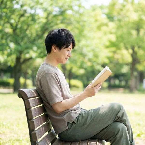 Man relaxing on a park bench and reading a book.