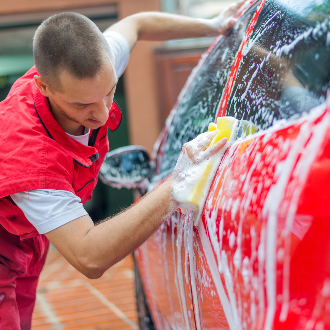 man using a sponge to spread soap on a car.