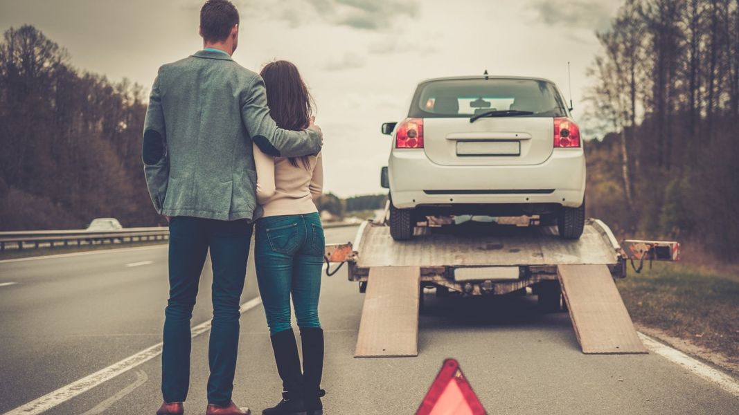 A couple stands on the side of the road as their car is loaded on to a tow truck A couple stands on the side of the road as their car is loaded on to a tow truck