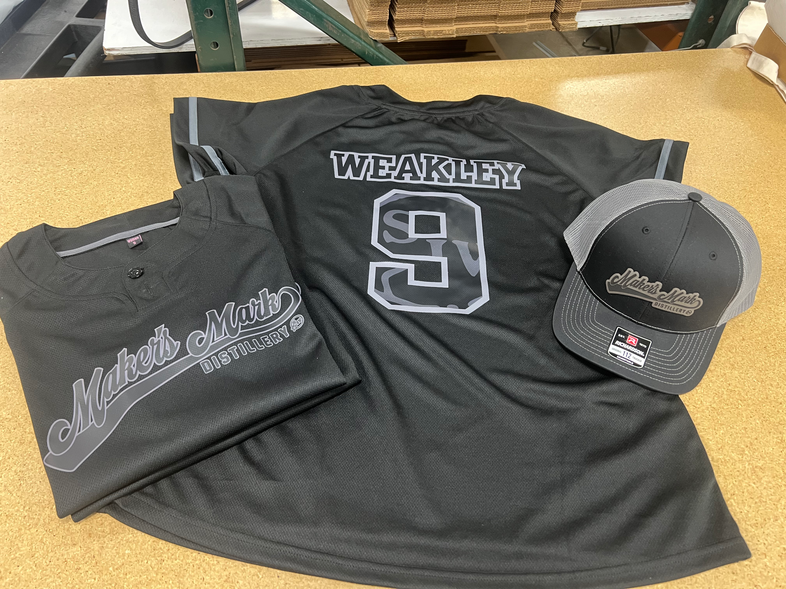 two gray baseball jerseys on a table with a baseball hat all with similar branding IMG_1258.png