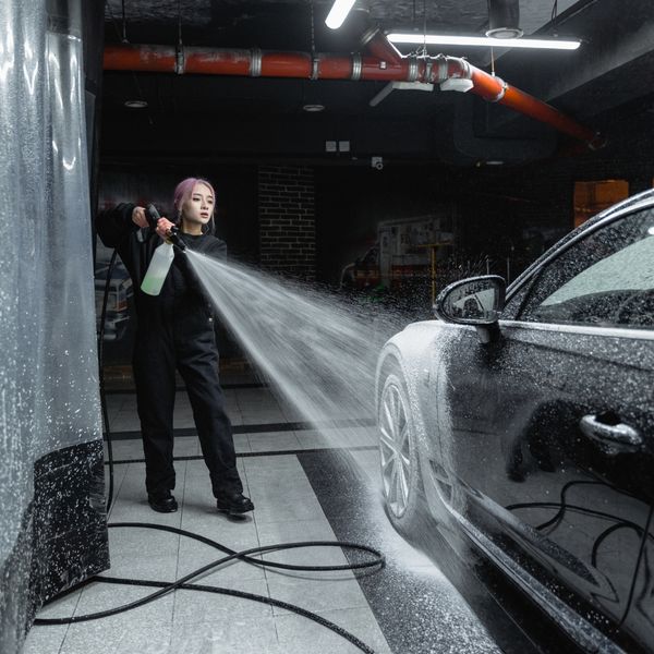 A woman spraying soap on a black car