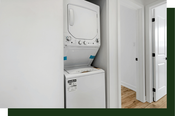 A compact laundry area or hallway nook featuring a stacked white washer and dryer unit next to an open doorway.